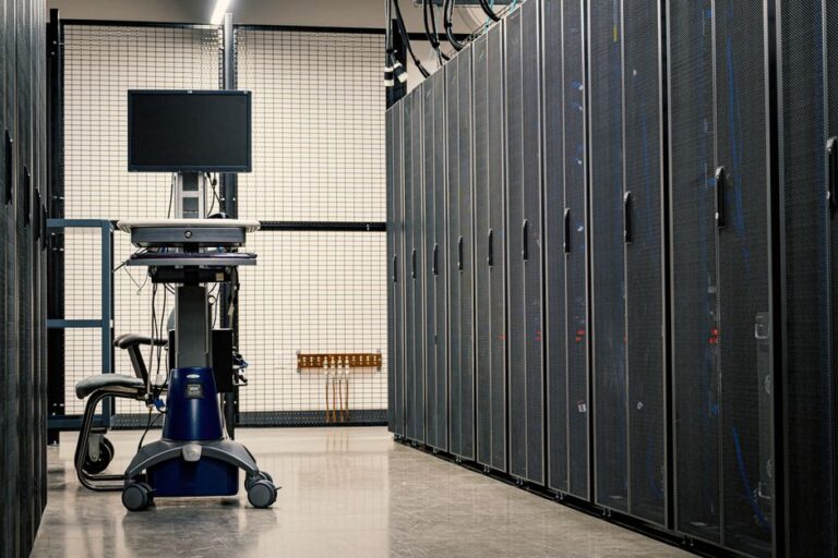 macOS Tahoe 26.2 : quatre Mac Studio en grappe IA, le M5 attend son câble Contemporary computer on support between telecommunication racks and cabinets in modern data center