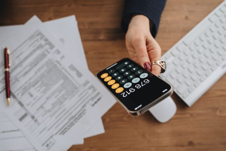 App Fichiers sur iPhone : 7 astuces pour ranger ses documents Hand holding smartphone calculator over tax documents on desk.