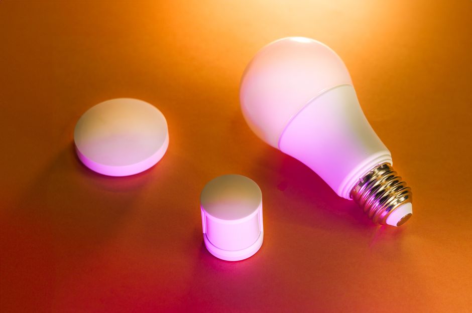Illuminated LED smart bulb with accessories on a vibrant orange background.
