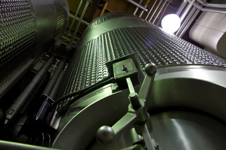 Low-angle shot of large stainless steel tanks inside a modern industrial facility.