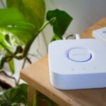 Philips Hue dépasse 100 produits en 2025 : le jardin clos change d’ampoule Philips smart hub beside a leafy plant in a stylish indoor setting, showcasing modern home automation.