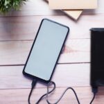 Smartphone charging with a power bank on a wooden desk, showcasing modern technology essentials.