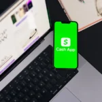 Apple et WeChat : 15 % sur les Mini Games chinois, la caisse change Smartphone showing Cash App screen on laptop keyboard, next to glasses and notebook.