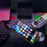 Stylish home entertainment setup featuring an iPhone, Apple TV, and gaming controller on a dark surface.