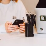 61 stickers Sneaky Sasquatch débarquent dans iMessage le 17 novembre 2025, Apple sort le grand jeu Young adult at a desk texting on smartphone, next to a laptop and stationery holder.