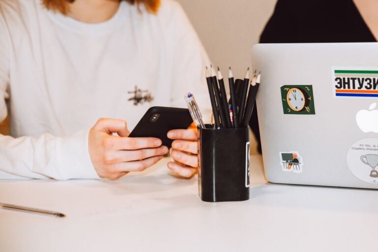 61 stickers Sneaky Sasquatch débarquent dans iMessage le 17 novembre 2025, Apple sort le grand jeu Young adult at a desk texting on smartphone, next to a laptop and stationery holder.