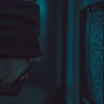 tvOS 26.2 disponible le 12 décembre 2025: mode enfants, Apple desserre la laisse A close-up of a blindfolded man facing a static television screen in a dark room.