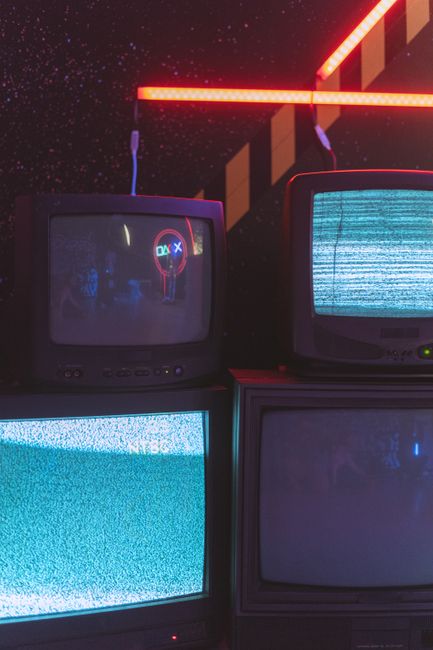 A collection of old CRT televisions displaying static noise under vibrant neon lighting.