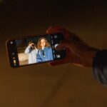 iPhone 2026 : la RAM flambe, Apple garde un joker A couple capturing a romantic memory using a smartphone camera during nighttime indoors.
