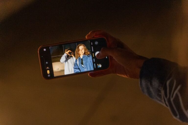 iPhone 2026 : la RAM flambe, Apple garde un joker A couple capturing a romantic memory using a smartphone camera during nighttime indoors.