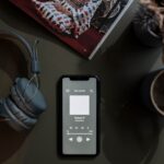Apple Podcasts s’ouvre seul sur iPhone et Mac : le lien qui inquiète A flat lay image of a smartphone playing a podcast next to headphones and a mug.