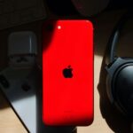 Fortnite reste hors de l’iPhone au Japon en 2025, les frais d’Apple coincent le retour A flat lay of a red iPhone surrounded by AirPods and Bose headphones on a wooden surface.