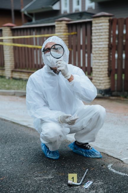A forensic investigator in protective gear examines a crime scene with a magnifying glass.