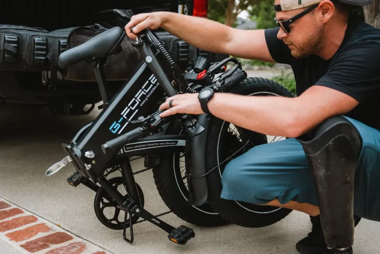 Ride1Up Portola à 1 095 dollars : pliable, mais 27 kg à porter A man folds a G-Force electric bike next to a truck, emphasizing outdoor lifestyle and convenience.