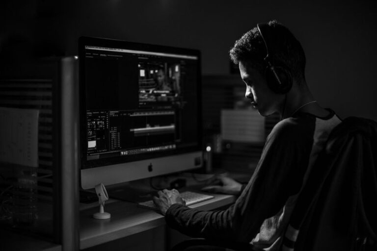 Aiarty Video Enhancer 3.0 sur Mac : le 4K sans magie A man wearing headphones working on video editing on a computer in a dimly lit office.