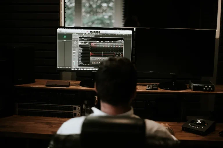 Studio Display : le bug macOS Tahoe dure depuis septembre 2025, le flash s’accroche A man with short hair sits at a desk with dual monitors in an editing studio.