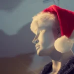 A mannequin dressed in a Santa hat in an indoor store window display, capturing a festive winter theme.