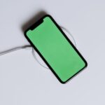 A minimalist smartphone with a green screen on a wireless charger, ideal for tech mockups.