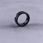 Pebble Index 01 : 75 dollars en précommande, zéro recharge A modern black smart ring with visible circuitry resting on a textured concrete surface.