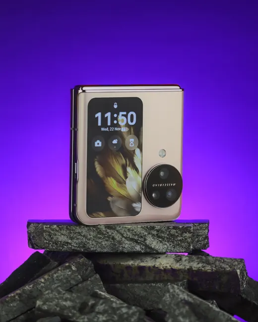 A modern foldable smartphone with a sleek design rests stylishly on textured rocks with a vibrant background.