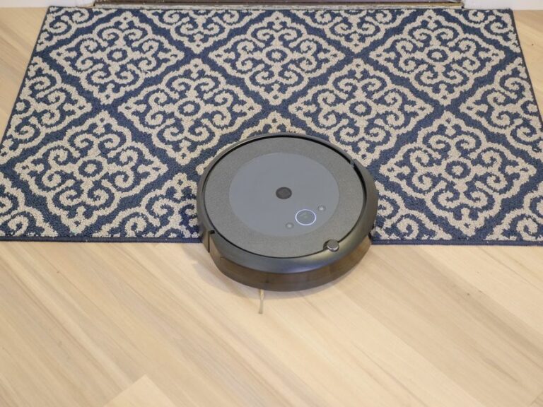 iRobot Roomba change de mains en 2025 : Apple Home au pied du mur A modern robotic vacuum cleaning a stylish patterned carpet on a wooden floor.