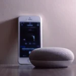 Radio sur HomePod en 2026 : Siri ne suit pas vos stations A modern smart speaker and smartphone on a wooden table, indoors.