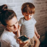 A mother and her child engaging with a smartphone indoors, depicting modern parenting and technology use.