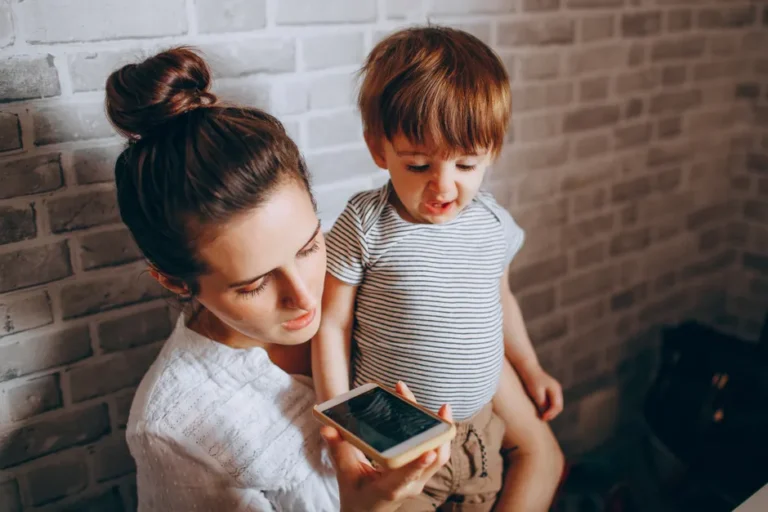 App Store et contrôle d’âge : le projet américain de 2025 a un angle mort A mother and her child engaging with a smartphone indoors, depicting modern parenting and technology use.