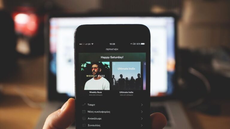 Apple Music dans ChatGPT : le DJ IA annoncé le 16 décembre 2025, sans date de sortie A person holding a smartphone with music streaming app in front of a laptop screen indoors.