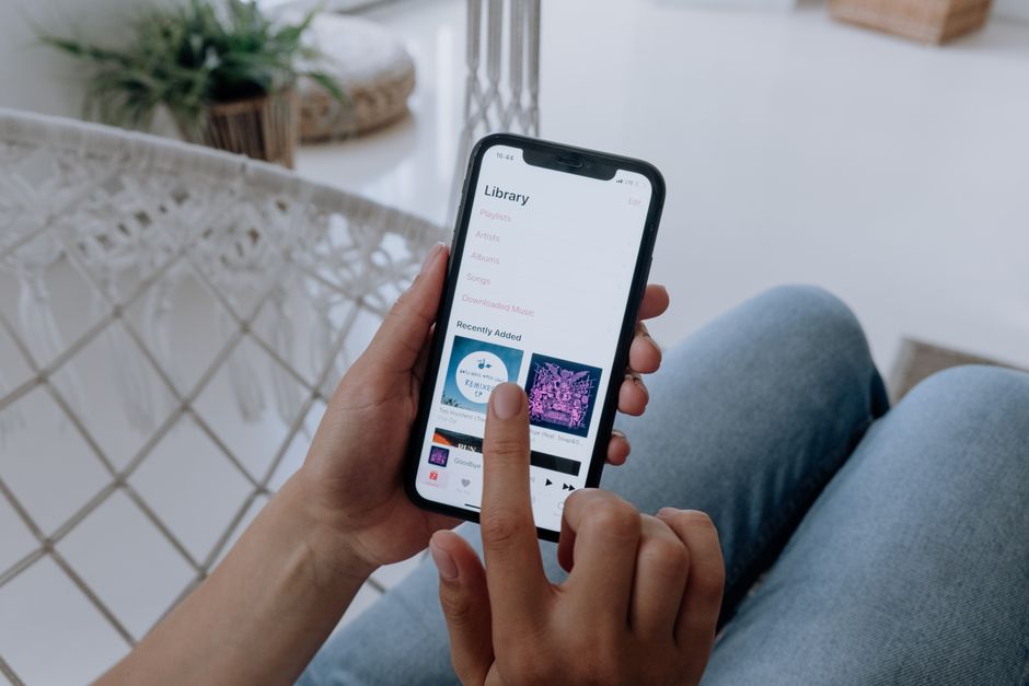 A person in jeans using a smartphone to browse a music app indoors.