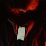 ICEBlock retirée de l'App Store en octobre 2025 : Apple sous pression A person using a smartphone in dim, moody lighting with a dark background.