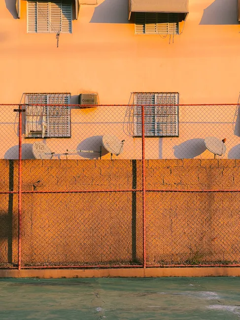 A residential building with satellite dishes and a chain-link fence under evening light.