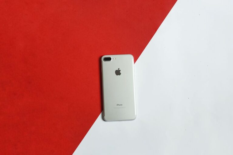iPhone 18 Pro attendu en septembre 2026 : Face ID sous l’écran, mais pas sans trou A silver smartphone placed on a contrasting red and white background captured from above.