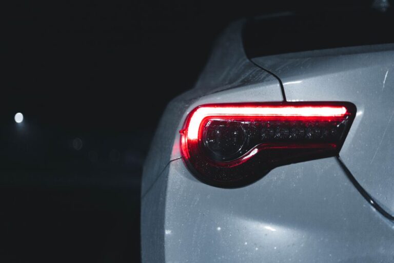 Apple Car : vitres adaptatives et feux-écrans, les brevets de 2019 et 2021 A sleek car's illuminated tail light with water droplets at night, showcasing modern automotive design.