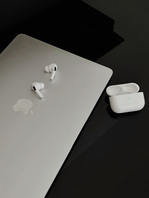 A sleek composition featuring AirPods Pro and MacBook on a dark surface, showcasing minimalist design.