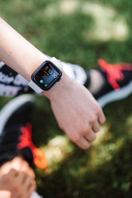 A smartwatch displaying time and apps on a person's wrist outdoors, with sporty shoes visible.