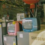 A storefront display featuring vintage televisions and home appliances on a sunny day in Bangkok.