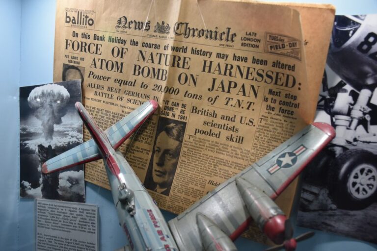 Pluribus : la bombe du final et les cookies de Tim Cook A vintage newspaper with an atomic bomb headline displayed alongside a model airplane and historic photos.