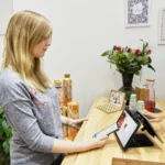 iPad 11 à 279 dollars le 16 décembre 2025 : le stock tranche A woman uses a tablet to make a payment in a stylish Berlin store, featuring modern decor and eco-friendly products.