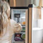 Pub Pluribus : le frigo n'a pas ciblé Carol, la blague a circulé Back view of a blonde woman retrieving food from a refrigerator in a bright kitchen.
