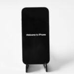 iPhone 18 Pro : Face ID sous l'écran, mais pas sans trou Black iPhone displayed on a stand with 'Welcome to iPhone' text against a white background.