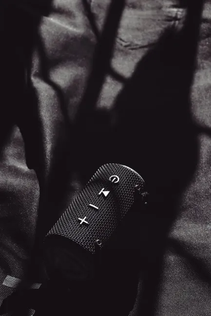 Black portable speaker resting on a textured fabric surface with artistic shadows.