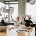 Paramount maintient son offre à 30 dollars pour Warner, Netflix visé Business team throwing papers in the air in a modern office, celebrating success.