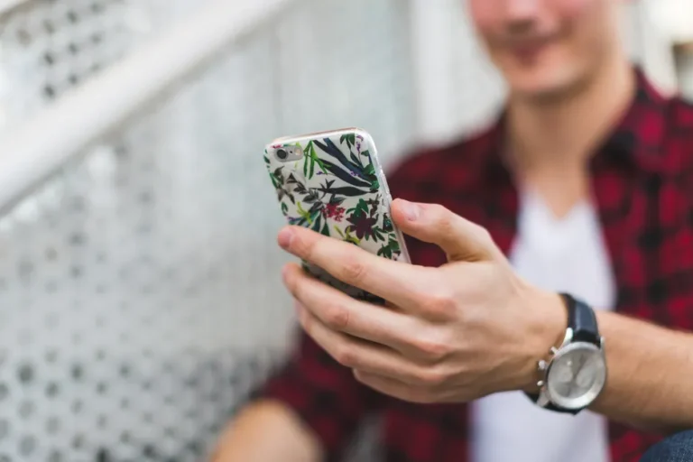 Coque iPhone 17 Pro : six modèles et le piège des tailles Close-up image of a person holding a smartphone in a floral case, focusing on lifestyle and technology.