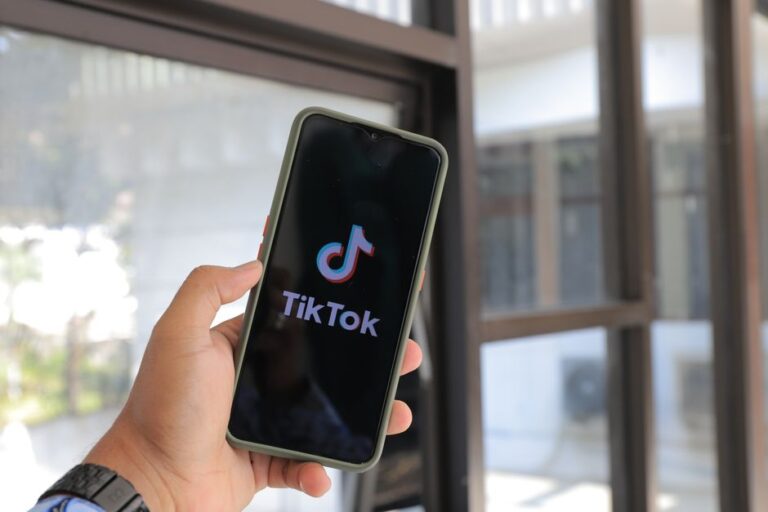 TikTok aux États-Unis : le deal du 22 janvier 2026, l’algo garde la clé Close-up of a hand holding a smartphone displaying the TikTok app indoors.