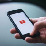 iPhone 17 : Apple pourrait rester numéro un des ventes jusqu'en 2029, Android garde le royaume Close-up of a hand holding a smartphone displaying the YouTube app on the screen.