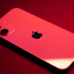 Close-up of a red smartphone with dual lenses on a red backdrop, highlighting sleek design and technology.