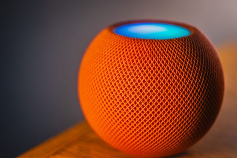 Apple imagine un écran en tissu pour le HomePod, sans mini-TV Close-up of an orange smart speaker with a glowing blue light, showcasing modern technology.