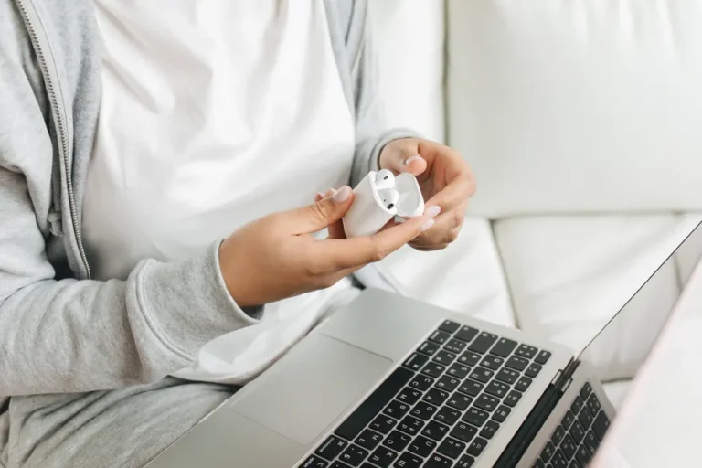 AirPods 4 ANC à 99 dollars le 1er décembre 2025: Apple tousse Close-up of hands opening wireless earbuds case near a laptop on a white couch.