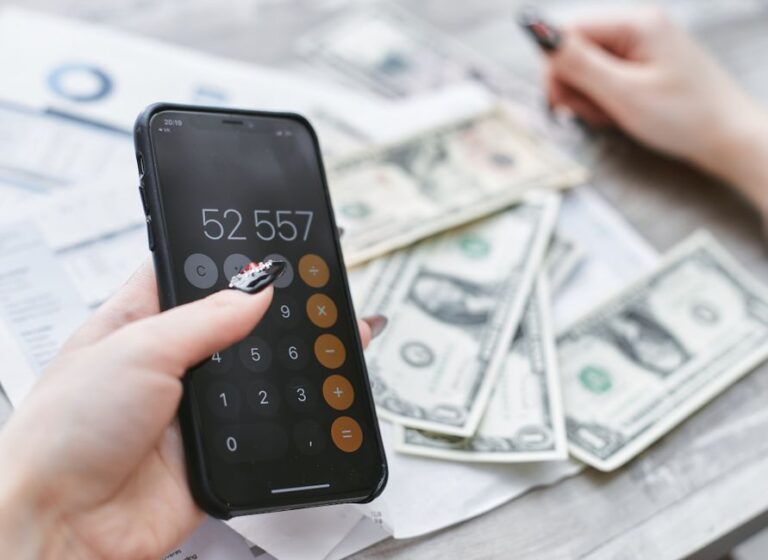 Black Friday 2025 : iPhone 17 Pro à 0 dollar chez AT&T, mais le forfait mord Close-up of hands using smartphone calculator next to dollar bills on table. Financial planning concept.